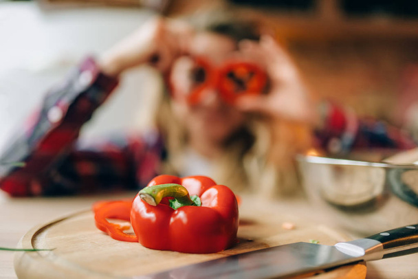 Молодая домохозяйка в фартуке балуется красным перцем на кухне. Женщина-повар делает здоровую вегетарианскую еду, салат приготовления
 - Фото, изображение