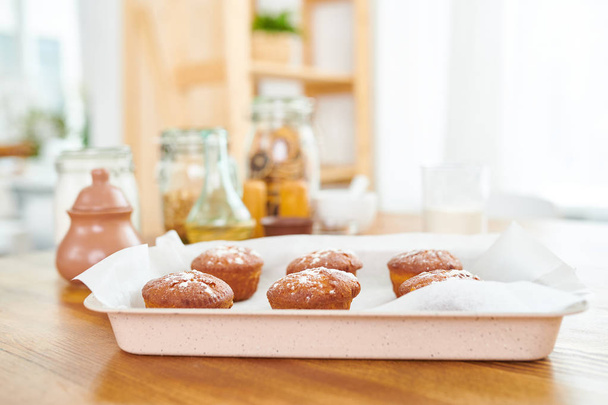 Hintergrundbild von frischen goldbraunen Muffins in Backblech auf Holztisch in gemütlich warmer Küche - Foto, Bild