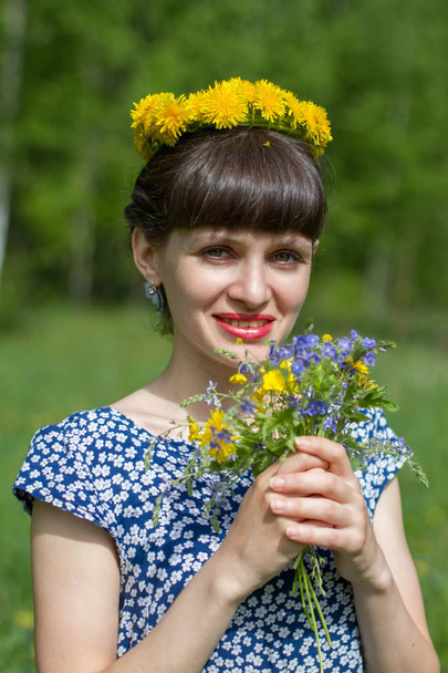 Beautiful girl in the Park in a wreath of dandelions and a bouquet of wild flowers - Foto, Imagem