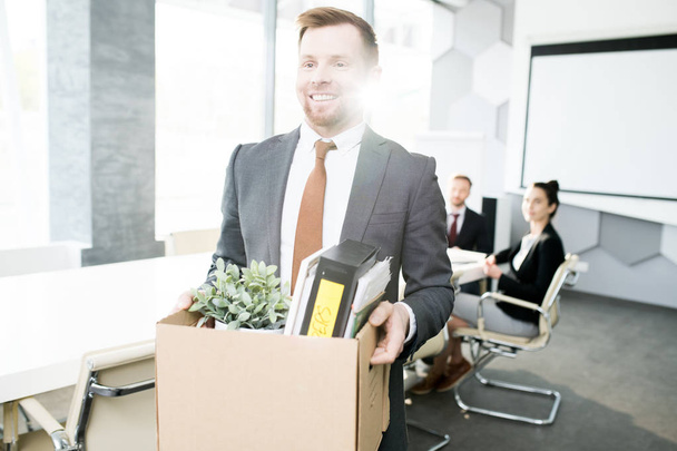 Waist up portrait of happy young man holding box of personal belongings leaving office after quitting job - Фото, изображение