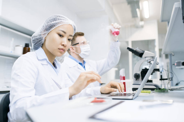 Портрет двух современных ученых, изучающих вещества во время работы над исследованиями в медицинской лаборатории, акцент на молодой азиатской женщине впереди
 - Фото, изображение