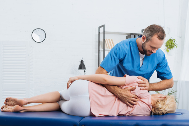 Lächelnder Chiropraktiker massiert Rücken eines Patienten, der im Krankenhaus auf Massagetisch liegt - Foto, Bild