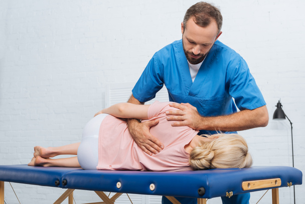 Portret van chiropractor masseren achterkant patiënt die liggend op een massagetafel in ziekenhuis - Foto, afbeelding