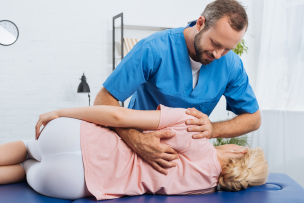 portrait d'un chiropraticien souriant massant le dos d'un patient allongé sur une table de massage à l'hôpital
 - Photo, image