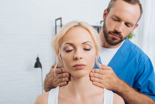 portrait of massage therapist massaging neck of young woman in clinic - Photo, Image