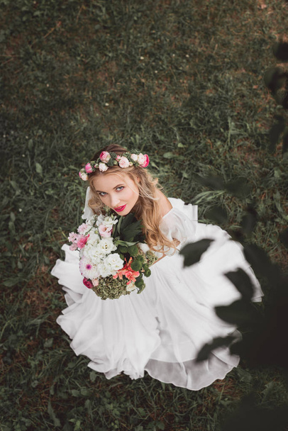 overhead view of beautiful young bride holding bouquet of flowers and looking at camera - Φωτογραφία, εικόνα