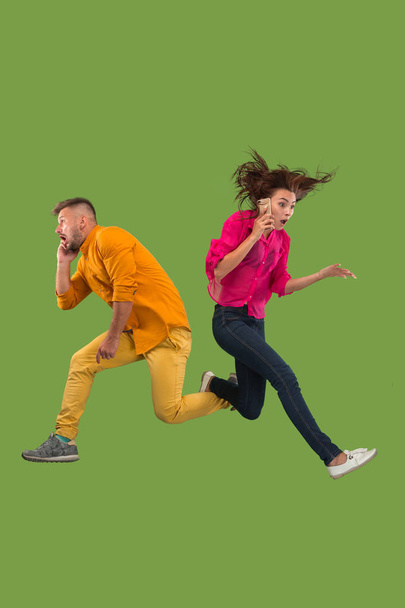 Full length of young couple with mobile phone while jumping - Foto, afbeelding