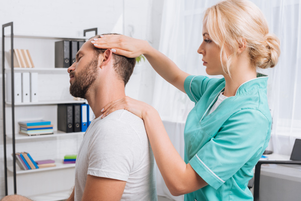 Zijaanzicht van vrouwelijke massagetherapeut massage van de nek doen aan patiënt in kliniek - Foto, afbeelding