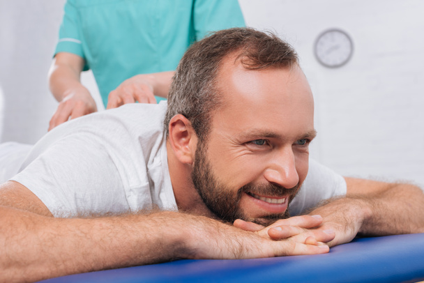 vue partielle du massothérapeute faisant le massage au patient souriant sur la table de massage à la clinique
 - Photo, image
