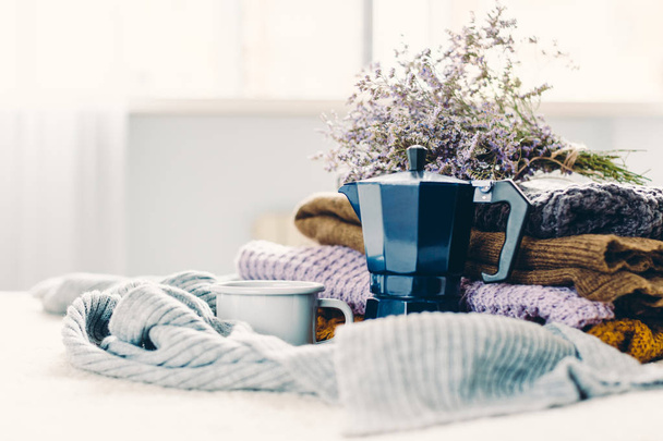 Koffie mok en blauw geiser koffie pot op een witte coverlet, een stapel van gebreide kleding en een sjaal - Foto, afbeelding