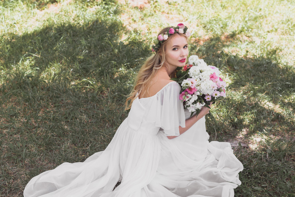 vysoký úhel pohled krásná mladá nevěsta ve svatebních šatech drží kytici květin a při pohledu na fotoaparát - Fotografie, Obrázek