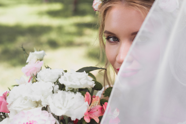 美しい若い花嫁ベールの花の花束を押しながらカメラ目線で  - 写真・画像