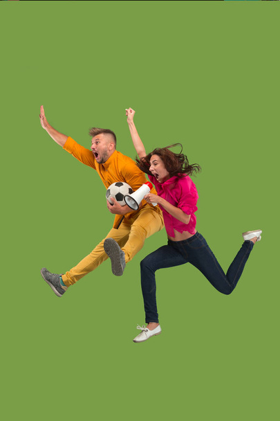 Forward to the victory.The young couple as soccer football player jumping and kicking the ball at studio on a green - Foto, Imagem