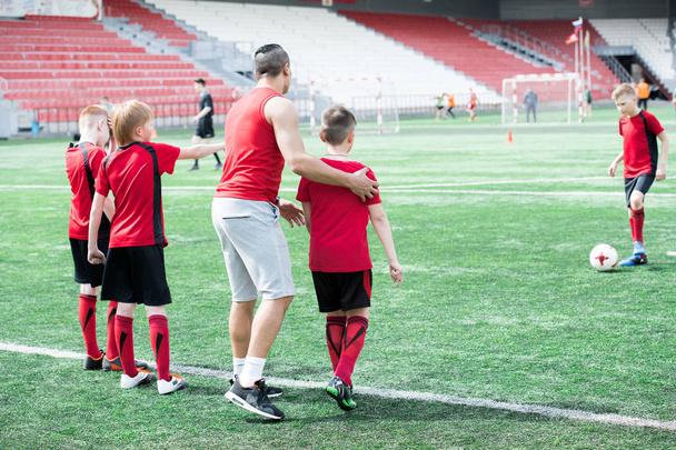 Ολόσωμο πορτρέτο του Τζούνιορ ποδοσφαιρικής ομάδας εξάσκηση στο υπαίθριο γήπεδο με τον νεαρό προπονητή - Φωτογραφία, εικόνα
