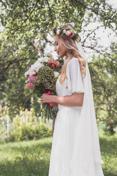 side view of smiling young bride holding wedding bouquet in park - Φωτογραφία, εικόνα