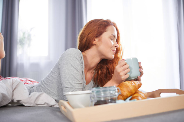 Beautiful happy redhead woman having breakfast in bed - 写真・画像