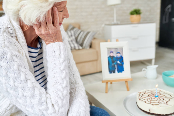 Baş taraftan yaslanmış ve düşünceli pastaya bir mum fotoğraf ile geçmiş hatırlama kocası ile görünümlü ve yumuşak hırka üzücü yalnız yaşlı kadın - Fotoğraf, Görsel