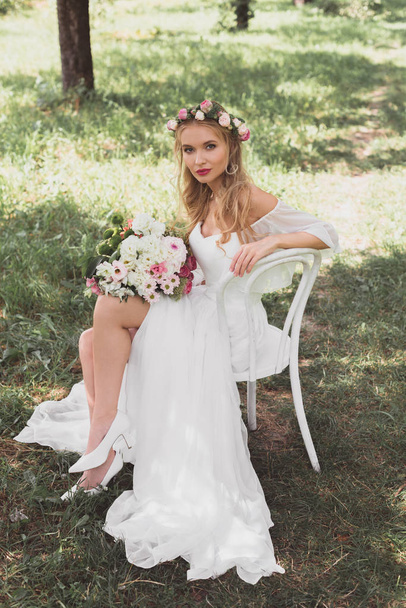 Hochwinkelaufnahme der schönen jungen Braut, die auf einem Stuhl sitzt und im Freien in die Kamera schaut - Foto, Bild
