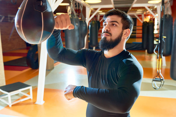 Brutal entraînement sportif barbu dans la salle de gym et sac suspendus de poinçonnage l'air confiant
 - Photo, image