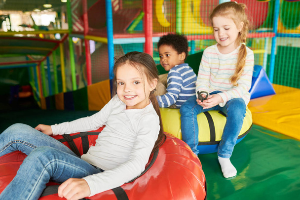 Портрет щасливих дітей, що сидять у пончиках, насолоджуючись слайдами у веселому дитячому центрі
 - Фото, зображення