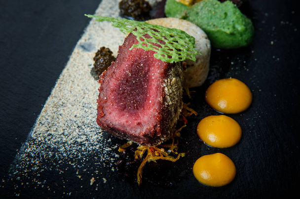макро два куска жареного мяса украшены пюре и соусом на черной тарелке на деревянном столе в ресторане
 - Фото, изображение