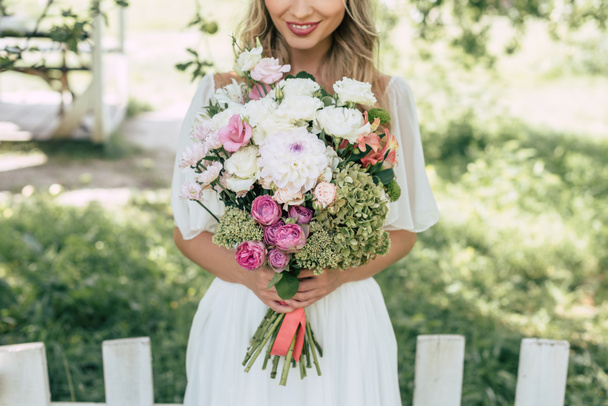 cropped shot of happy blonde bride holding beautiful wedding bouquet outdoors - Foto, afbeelding
