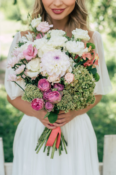 cropped shot of smiling blonde bride holding beautiful wedding bouquet  - 写真・画像