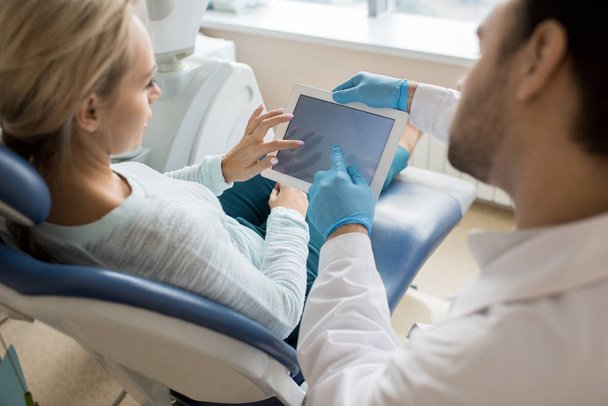Vue de dos de la femme ayant une réunion avec le dentiste et regardant la présentation sur tablette assise dans la chaise
.  - Photo, image