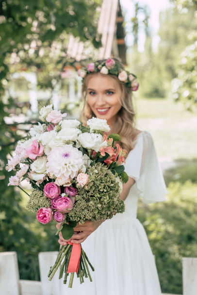 close-up view of happy young bride holding beautiful wedding bouquet outdoors - Фото, изображение