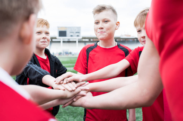 Retrato do time de futebol júnior empilhando mãos durante conversa motivacional antes do jogo no estádio ao ar livre, espaço de cópia
 - Foto, Imagem