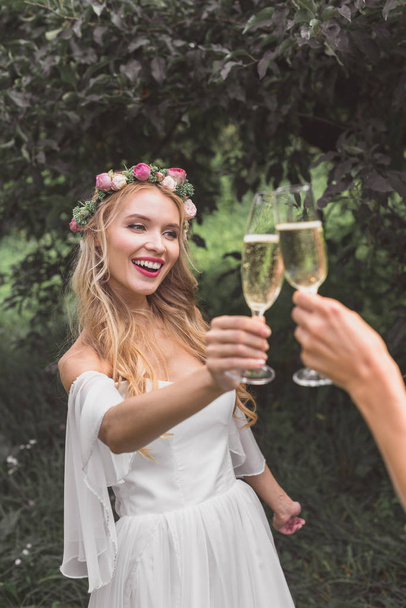 partial view of happy young bride clinking glasses of wine with someone in park   - Foto, Imagen