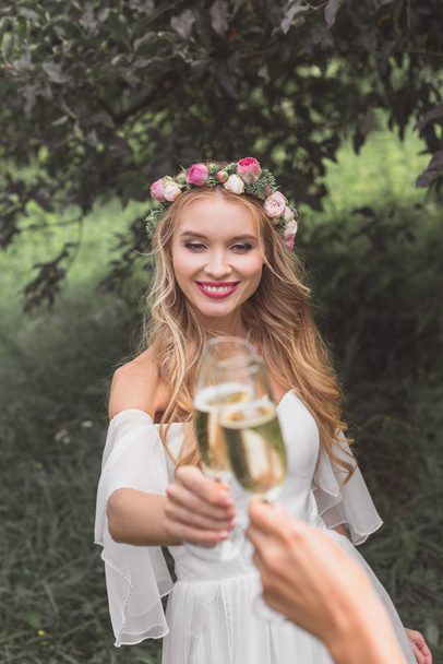 belle jeune mariée souriante cliquetis verres de champagne avec quelqu'un dans le parc
  - Photo, image