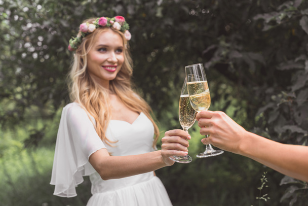 tiro cortado de feliz jovem noiva clinking copos de champanhe com alguém no parque
   - Foto, Imagem