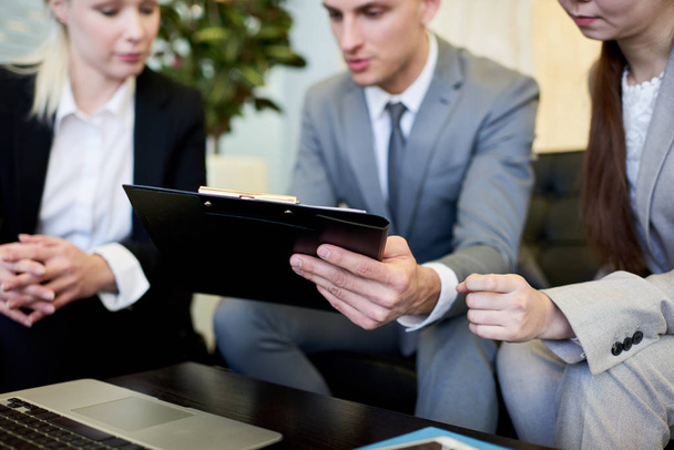 Close up de empresário segurando prancheta mostrando documento para colegas em reunião de equipe
 - Foto, Imagem
