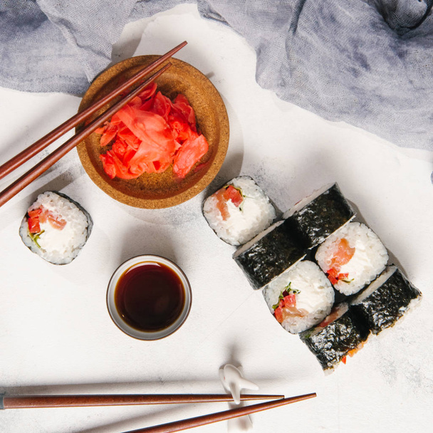 Rollos tradicionales japoneses con salmón y queso crema servidos con palillos, salsa de soja y jengibre sobre fondo de piedra gris claro
 - Foto, imagen