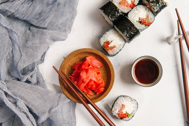 Rollos tradicionales japoneses con salmón y queso crema servidos con palillos, salsa de soja y jengibre sobre fondo de piedra gris claro
 - Foto, Imagen