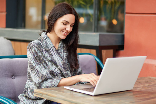 Успешная молодая деловая женщина работает на ноутбуке, проверяет базу данных на почтовый ящик, использует беспроводной интернет в уютном кафе, современный ноутбук компьютер, имеет положительное выражение. Технологии
 - Фото, изображение