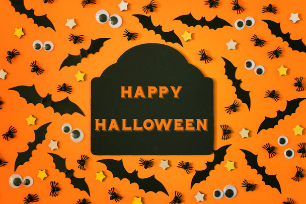В центре находится фигурная табличка с надписью. Счастливого Хэллоуина. Многие декоративные пауки, кукольные глаза и летучие мыши облицованы оранжевым фоном
. - Фото, изображение