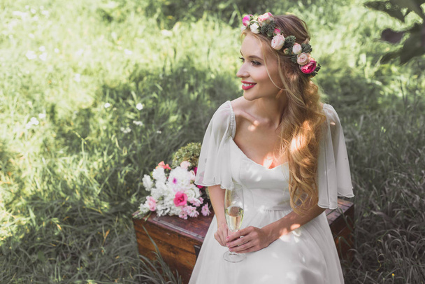 высокий угол обзора улыбающейся молодой невесты, держащей бокал шампанского и сидящей на винтажной груди
 - Фото, изображение