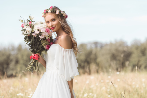 beautiful young bride holding wedding bouquet and smiling at camera outdoors   - Photo, Image