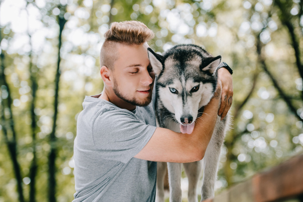 молодий чоловік обіймає хаскі собаку в парку
 - Фото, зображення