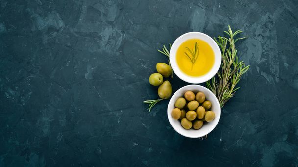 A set of olives and olive oil and rosemary. Green olives and black olives. On a black stone background. Free space for text. - Photo, image