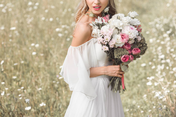cropped shot of young blonde bride in wedding dress holding beautiful bouquet of flowers outdoors - Foto, imagen