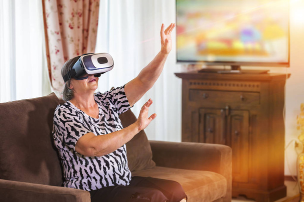 Старшая женщина с виртуальной гарнитурой или 3D очками играет в видеоигру дома. Технологии, дополненная реальность, развлечения и концепция людей. Сосредоточься на ее руках.
! - Фото, изображение