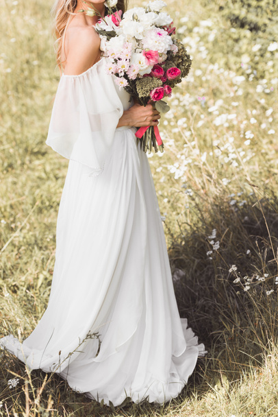 oříznuté shot z nabídky mladá nevěsta ve svatební šaty drží krásnou kytici květin venku - Fotografie, Obrázek