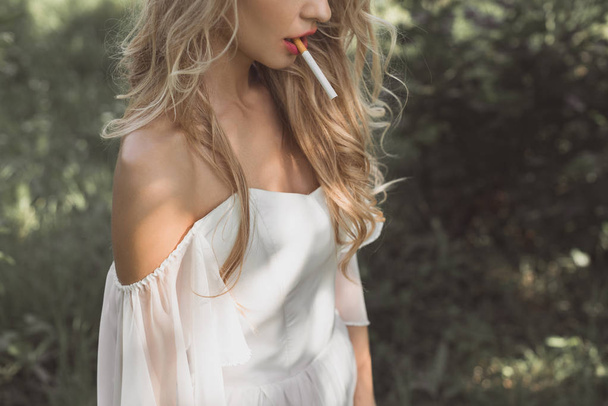 cropped shot of young blonde woman in white dress smoking cigarette outdoors - Fotoğraf, Görsel