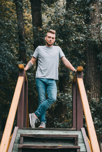 handsome man posing on stairs in park and looking at camera - Zdjęcie, obraz