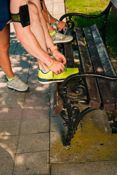 Happy young sporty couple tying shoelaces outdoors - Photo, Image