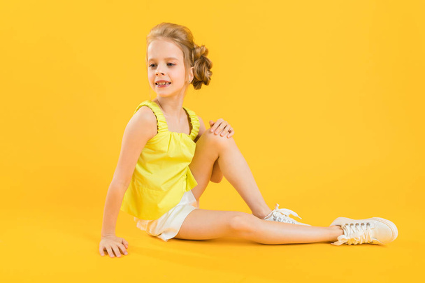 A teenage girl is sitting on a yellow background. - 写真・画像