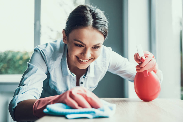 Young Smiling Woman in Gloves Cleaning House. Happy Beautiful Girl wearing Protective Gloves Cleaning Desk by spraying Cleaning Products and wiping with Sponge. Woman Cleaning Apartment - Photo, image